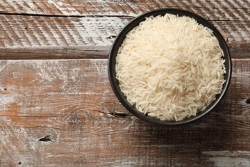 Raw basmati rice in bowl on wooden table, top view. Space for text