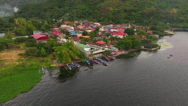 Parking traditional boats at shore in front of asian village at Taal Lake, Philippines. Aerial approaching shot,