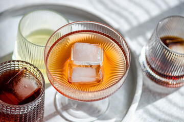 Top view of assortment of textured glasses filled with various alcoholic drinks, highlighting a prominent glass with a large ice cube