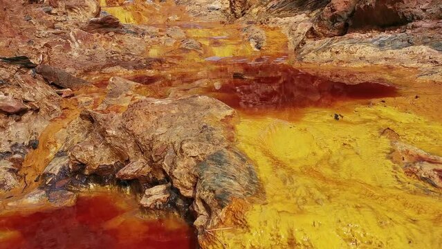 Panning of the stream of reddish water between rocks of the Rio Tinto near its source, Huelva