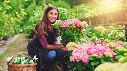 Fototapeta na wymiar Happy smiling young gardener selecting hydrangea plants in a nursery in the sun