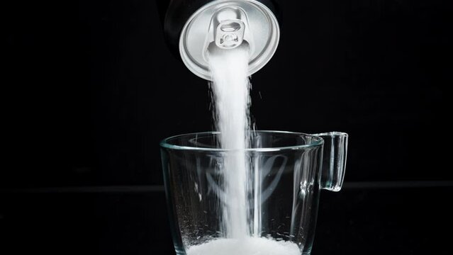 Sugar Is Poured into a Glass from a Soda Can on a Black Background, Isolated. Harmful Drinks. Slow-Motion.