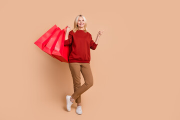Full length photo of positive sweet woman wear red sweater rising shoppers pointing empty space isolated beige color background