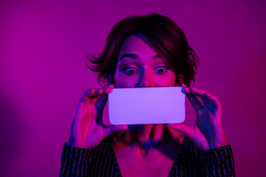 Photo of pretty young girl cover mouth white screen look down dressed stylish overall outfit isolated on neon light pink color background