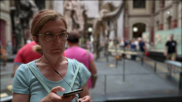 Berlin, Germany, August 10, 2023. At the natural science museum a middle-aged woman is absorbed in listening to the audio guide. Slow motion conceptual footage. People on the blurred background.