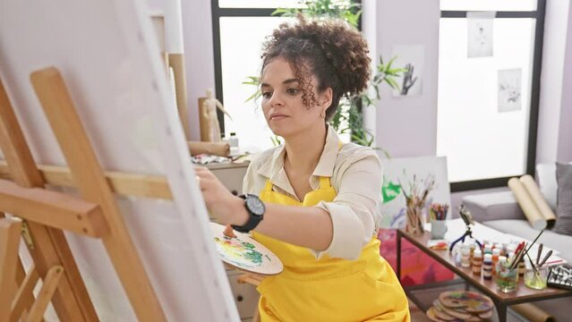 Worried hispanic curly hair artist woman staring at watch, fearing she's late for work at her studio