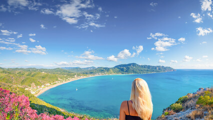 A blonde haired woman enjoys a view of the bay of Agios Georgios, Corfu, Greece.