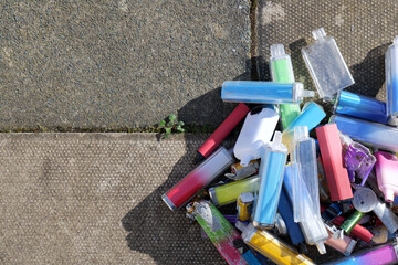 Discarded electronic cigarette vapes that have been collected from roads and pavements shot over a pale concrete slab background