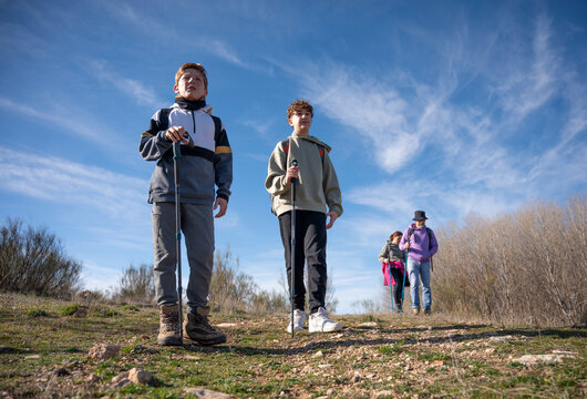 Low angle of two young individuals leading a family hike on a clear day, with two adults following behind on a rural trail