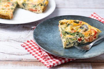 Italian Frittata made with spinach, tomatoes, onion and peppers on white wooden table