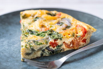 Italian Frittata made with spinach, tomatoes, onion and peppers on white wooden table. Close up