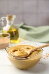 Spoon and glass bowl with tasty mustard sauce on white table