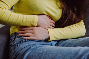Close up of unknown young woman suffering from menstrual pain. Girl with hands squeezing belly...