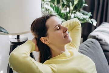 Close up of smiling peaceful young woman with closed eyes relaxing on comfy sofa at home, calm...