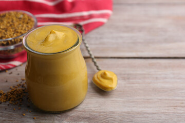 Jar and spoon with tasty mustard sauce on wooden table, space for text