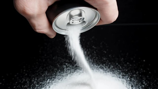 A mound of sugar spilled from a soda can on a black background. Slow-motion.