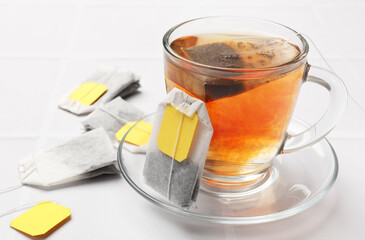 Tea bags and cup of aromatic drink on white table, closeup. Space for text