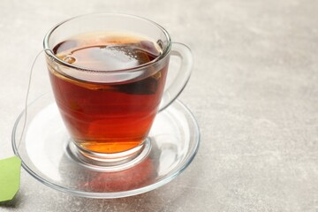 Brewing tea. Glass cup with tea bag on light table, closeup. Space for text