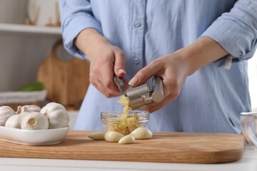 Woman squeezing garlic with press at white table in kitchen, closeup - obrazy, fototapety, plakaty