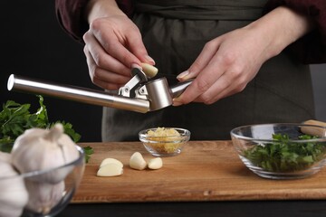 Woman squeezing garlic with press at black table, closeup - obrazy, fototapety, plakaty