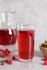 Tasty cranberry juice in glass and fresh berries on light grey table