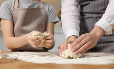 Making bread. Mother and her daughter kneading dough at wooden table indoors, closeup