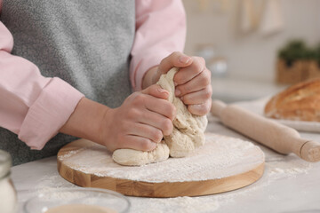 Making bread. Woman kneading dough at white table in kitchen, closeup