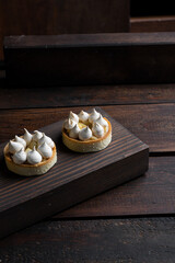 Tartlets with cream and meringue on a dark wooden background