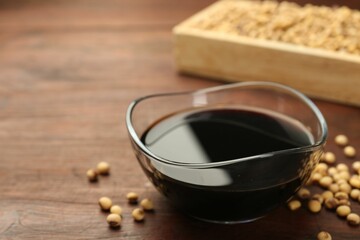 Soy sauce in bowl and soybeans on wooden table, closeup. Space for text