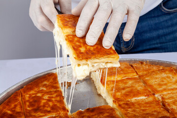 Turkish traditional pastry with cheese, su boregi. A hand holding a slice of cheesy pastry isolated...