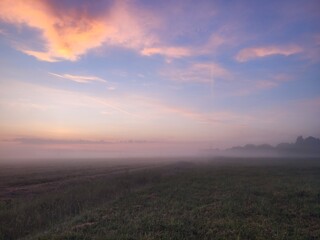 purple dawn against the backdrop of beautiful clouds in a field covered with fog