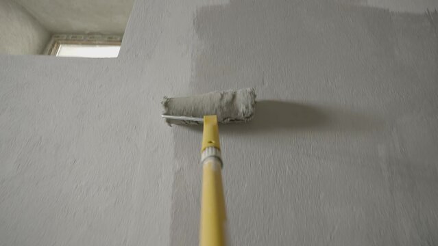 Painting Grey wall with paint roller . Close Up Shot of White Paint being applied on a wall. Room Renovations at Home concept. Painter man painting the wall in home. Camera attached to the brush	
