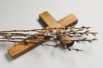 Wooden cross and willow branches on light grey background. Easter attributes