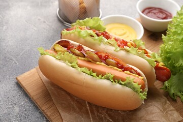 Delicious hot dogs with lettuce, onion and pickle served on grey table