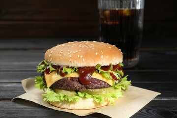 Burger with delicious patty and soda drink on black wooden table