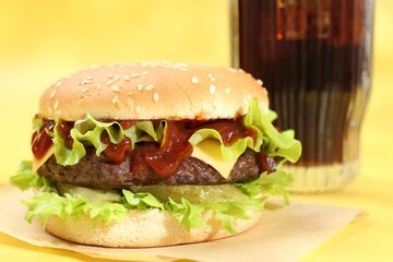 Burger with delicious patty and soda drink on yellow background, closeup