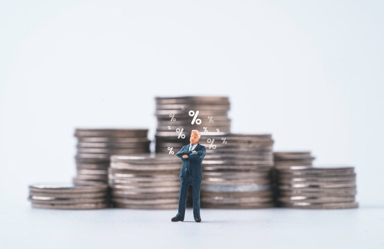 Businessman miniature figure standing with percentage sign and coins stacking for considering of increase or decrease interest rating to get dividend and profit concept.