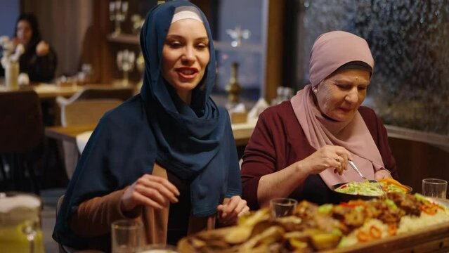 Muslim Mother and Daughter Having Dinner and Talking in a Restaurant in Ramadan or on Eid