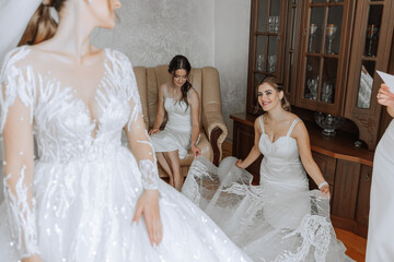 Bridesmaids rejoice in the morning, helping to fasten the buttons on the wedding dress and prepare...