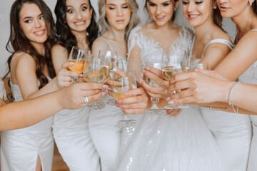 Photo with bridesmaids drinking champagne from glasses in the morning in a beautiful hotel. Photo of a beautiful young bride and her friends in matching dresses drinking champagne before the wedding.
