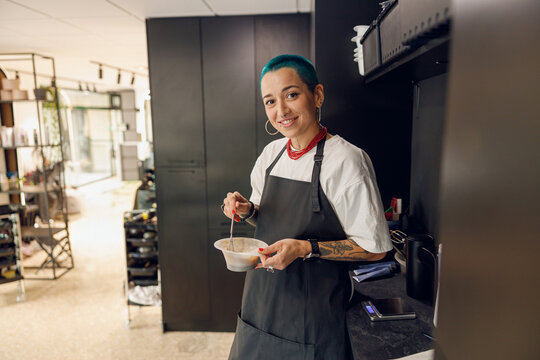 Stylist preparing a hair dye in a container and looks camera with smile. Hairdresser salon concept - Powered by Adobe