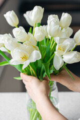 A woman touches a bouquet of white flowers in a vase, close-up.