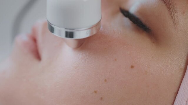 Woman on microcurrent face lifting therapy on cheek zone in cosmetology clinic.
