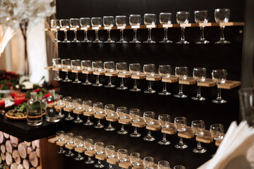 Champagne glass stand at a wedding party. Glasses for alcoholic drinks on a black wooden stand. Alcohol. Champagne. Celebration.