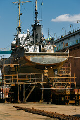 Shipyard workers engage in maritime vessel maintenance, restoring naval ship on dry dock against a...