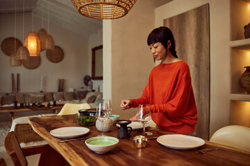 An Asian woman serving dinner at home, waiting for her friends.