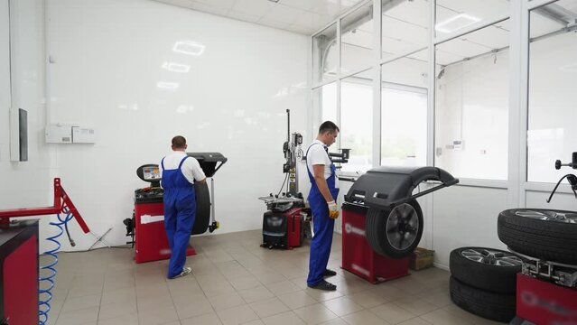 Auto techs work in tire shop, servicing vehicle wheels with changer, balancer tools. Uniformed workers remove, replace, balance tires in modern garage, ensuring automotive safety, efficiency.