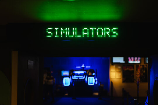 Green LED sign reading SIMULATORS in a dimly lit arcade room with neon blue lights in the background