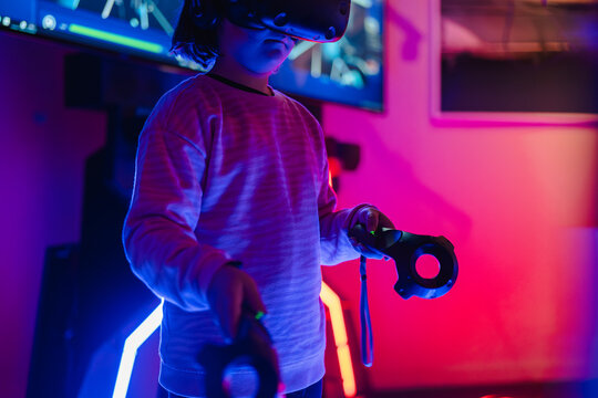 Child focused on playing with a VR headset and controllers in a room illuminated by neon gaming lights