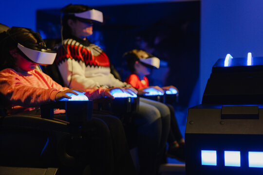 Row of focused individuals using VR headsets and hand controls in high-tech simulation seats with blue lighting